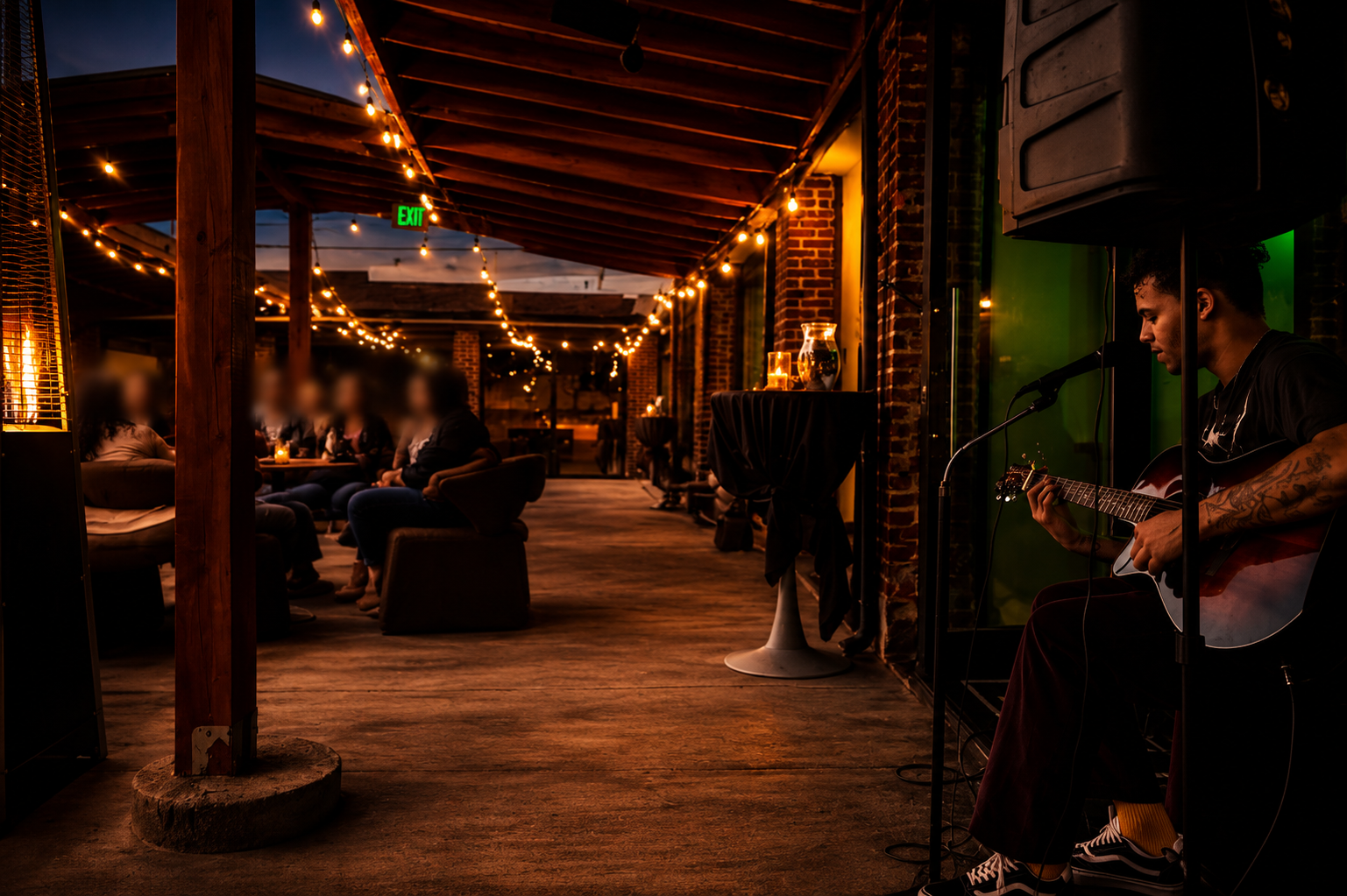 Live acoustic guitarist on Brick Bistro's covered courtyard at dusk with string lights and guests dining